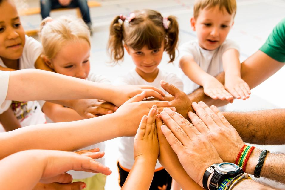 Kinder und Erwachsene legen ihre Hände in einem Kreis zusammen, symbolisieren Zusammenarbeit und Gemeinschaft.